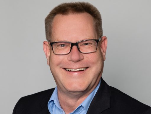 Portrait eines sympathisch lächelnden Mannes mit Brille, dunklem Anzug und hellblauer Hemd - Mitarbeiterfoto