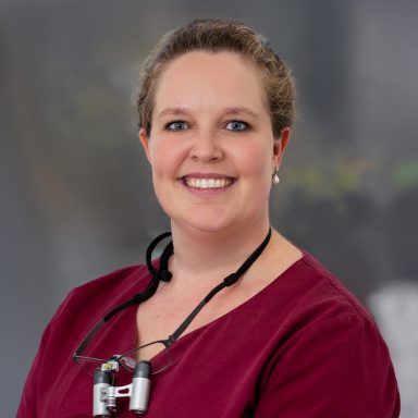 Zahnärztin in Arbeitskleidung mit Lupenbrille,die um den Hals gebunden ist